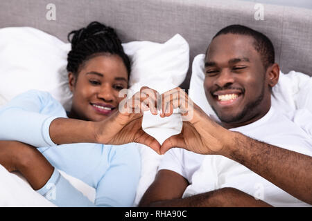 Happy African Couple Lying On Bed Making Heart Shape Stock Photo