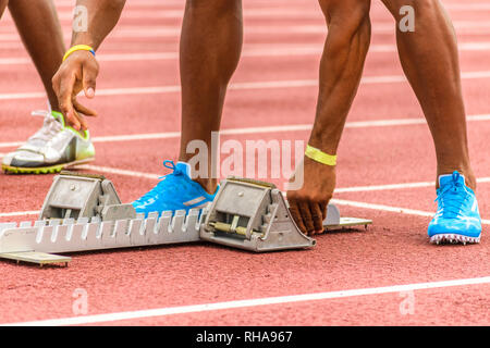 Starting blocks being adjusted by young black male athlete on outdoor track before start of race Stock Photo