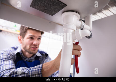 Young Male Plumber Repairing Sink Pipe With Adjustable Wrench Stock Photo