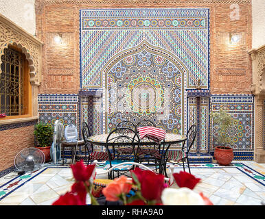 Inner courtyard with tiled walls and floor from mosaic. Traditional ornate and colorful arabesque wall carvings above an archway in Moroccan riad . Stock Photo