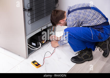 Side View Of A Male Repairman Checking Refrigerator With Digital Multimeter At Home Stock Photo