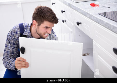 Smiling Handyman Fitting A New Door Under The Kitchen Worktop Stock Photo