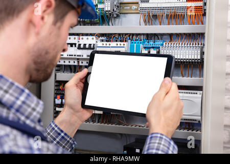 Technician Holding Digital Tablet With Blank Screen In Front Of Fuse Box Stock Photo