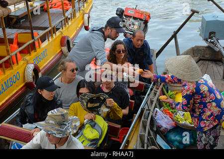 Phong Dien, Vietnam - December 31st 2017. A tourist on a boat tour considers buying fruit from a vendor at at the Phong Dien Floating Market near Can  Stock Photo