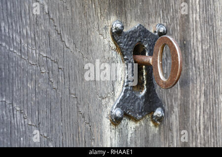 Closeup of an old key in a traditional keyhole lock and ancient wooden door