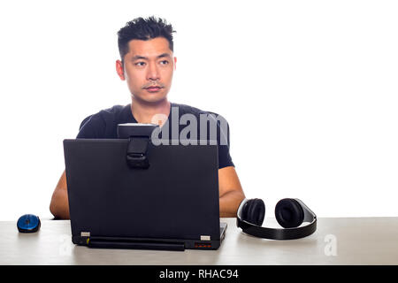 Asian male wearing headphones playing a video game and streaming online with a webcam on a laptop pc.  The image depicts entertainment industry and el Stock Photo