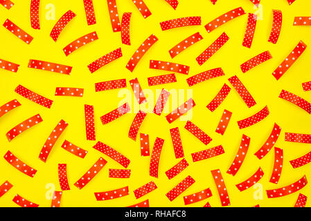 Pattern made from the red pieces of ribbons, isolated on a yellow background. View from the top. Stock Photo