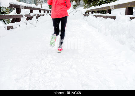 Young woman running on snow in winter mountains wearing warm clothing gloves in snow weather. Sport, fitness inspiration and motivation. Happy teen wo Stock Photo