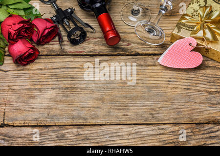 Valentines day concept. Wine bottle, red roses, gift box, corkscrew and glasses of wine on a rustic wooden blackboard with copy space for text. Stock Photo