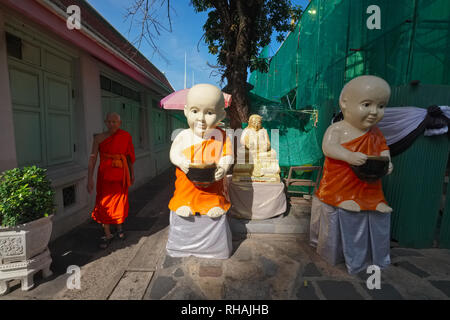 A Buddhist monk in the grounds of Wat Arun, Bangkok, Thailand, passing plastic figures of novice monks Stock Photo