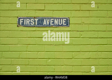 Vintage First Avenue street sign, on a green painted brick wall.  Sign is old and shows major sign of wear and some rust Stock Photo