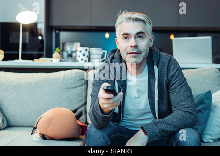 Grey-haired bearded attractive man in sportswear watching tv Stock Photo