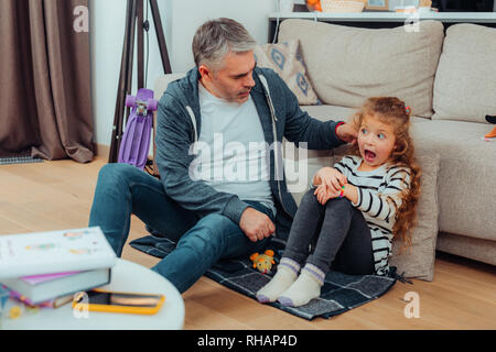Handsome grey-haired tall father with a red watch pulling his daughters ear Stock Photo