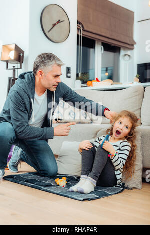 Handsome grey-haired tall father with a red watch talking strictly to his daughter Stock Photo