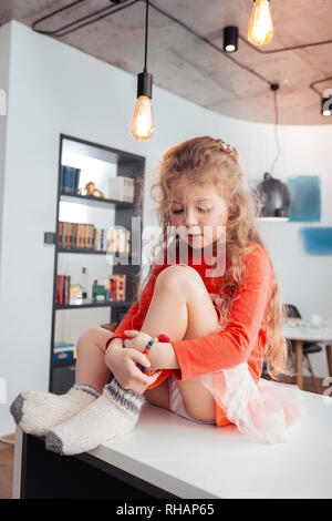 Cute small long-haired girl in a red dress looking through her fingers Stock Photo