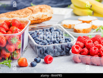 Plastic tray containers of fresh organic healthy beries and bread for fruit sandwiches. Blueberries, strawberries, bananas and raspberries on stone ki Stock Photo