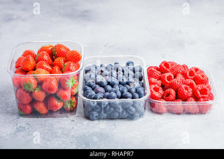 Plastic tray container of fresh organic healthy blueberries, strawberries and raspberries on stone kitchen table background. Stock Photo