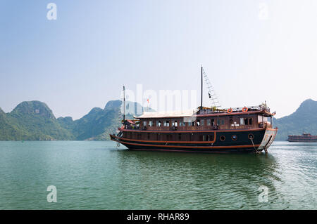 A wooden tourist junk boat anchored with large islands covered in vegetation in the background, Halong Bay, Vietnam Stock Photo