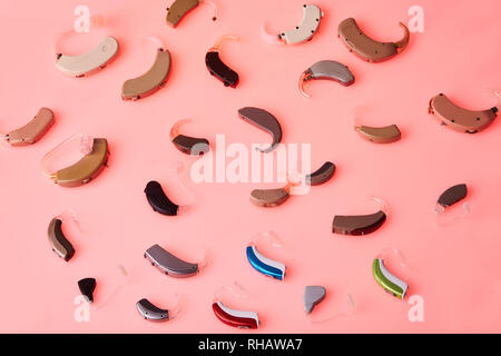 Different hearing aids on pink background, alternative to surgery. ENT accessory Stock Photo