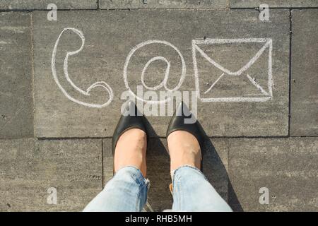 Female feet with contact symbols phone mail and letter, written on grey sidewalk, communication or contact us concept Stock Photo