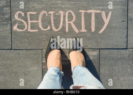 View from above, female feet with text security written on grey sidewalk Stock Photo
