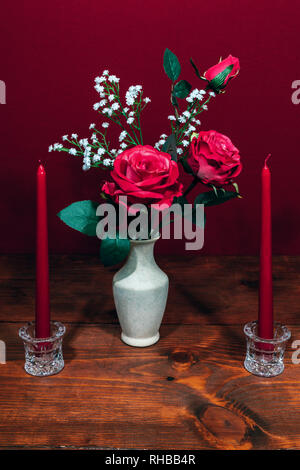 Beautiful pink roses in a vase acsented with Baby's Breath flowers, Two red candles in crystal holder. Stock Photo
