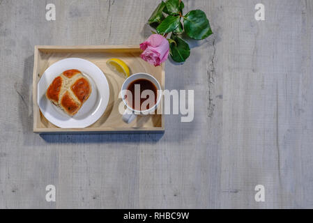 Flatbed, top shot of a tray with lemon tea and hot cross bun.  A beautiful single pink rose stem lying beside.  Situated on a third with copyspace. Stock Photo