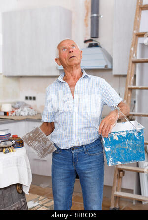 Elderly man with plastering tools looking at repairable room during renovation works Stock Photo