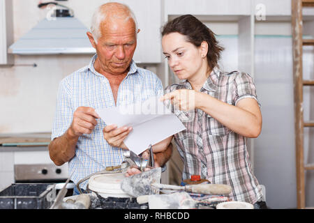 Confused woman with her elderly father reading work manual on mixer tap installation during overhaul at home Stock Photo