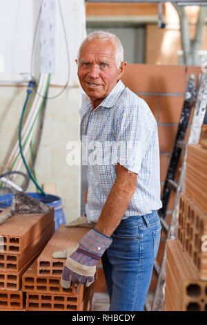 Skillful older man inspecting brick for installing wall in building under construction Stock Photo