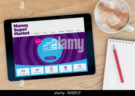 The MoneySuperMarket website features on an iPad tablet device which rests on a wooden table beside a notepad (Editorial use only). Stock Photo