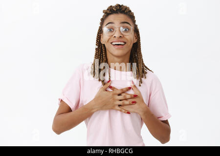 Waist-up shot of touched and happy passionate african american woman with dreadlocks in frames holding palms on heart sighing from love and admiration Stock Photo