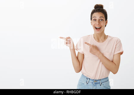 Waist-up shot of happy enthusiastic and excited joyful attractive european female with tan and messy hairbun smiling surprised and upbeat pointing Stock Photo
