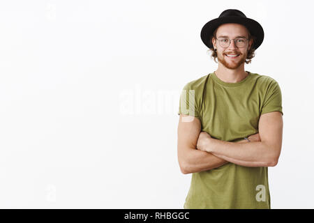 Friendly-looking delighted and calm handsome bearded male in glasses and hat smiling joyfully enjoying observing results of productive work holding Stock Photo