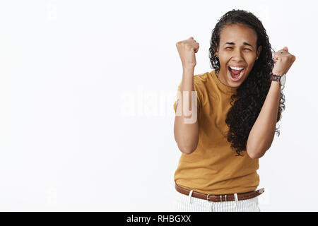 Waist-up shot of super excited astonished and happy joyful young african american woman raising clenched fists in success gesture screaming from Stock Photo