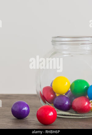 Multicolored large gumballs in cute jar and on wooden table Stock Photo