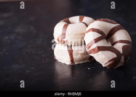 Striped donuts on dark wooden table. Delicious snack. Stock Photo