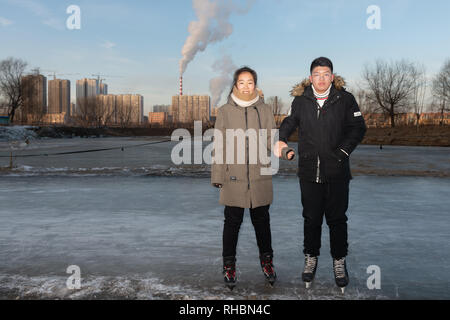 Young couple on skates, holding hands at an ice rink on the banks of the SongHua river, Jilin City Stock Photo