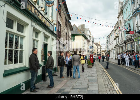 View along the busy and popular, historic Southside Street, Barbican, Plymouth with people enjoying colourful shops and pubs, with bunting overhead. Stock Photo