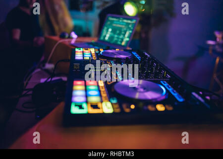 DJ plays live set and mixing music on turntable console at stage in the night club. Disc Jokey Hands on a sound mixer station at club party. DJ mixer Stock Photo