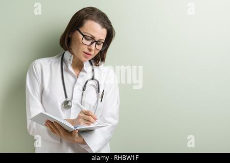 Smiling medical doctor woman with stethoscope taking notes on her notepad against green background Stock Photo