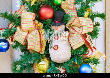 Christmas Winter December Holiday decor. Door Wreath with ribbons, shiny colorful metal decorative balls and a snowman teddy bear. Stock Photo