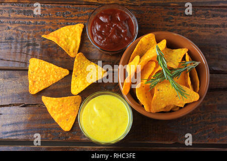 Nachos corn chips placed in ceramic bowl on wooden table next to assorted sauces Stock Photo
