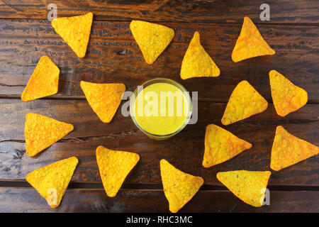 Nachos corn chips spread on wooden table next to assorted sauces Stock Photo