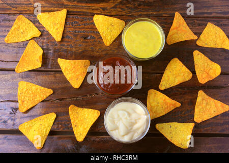 Nachos corn chips spread on wooden table next to assorted sauces Stock Photo