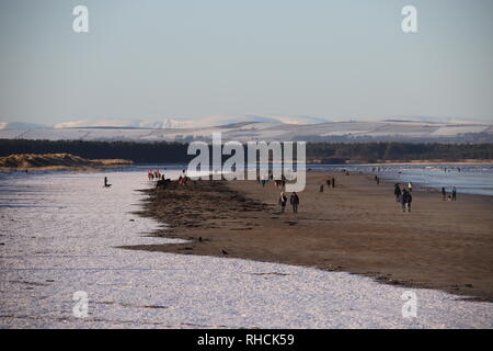 St Andrews, UK. 2nd February 2019. People walking on West Sands beach St Andrews after overnight snow with distant snow covered peaks in the Angus Glens.  © Stephen Finn/Alamy Live News Stock Photo