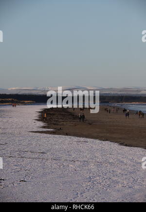 St Andrews, UK. 2nd February 2019. People walking on West Sands beach St Andrews after overnight snow with distant snow covered peaks in the Angus Glens.  © Stephen Finn/Alamy Live News Stock Photo