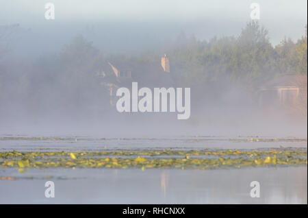 The autumn fog begins to lift revealing a north woods home on the shores of a wilderness lake in northern Wisconsin. Stock Photo