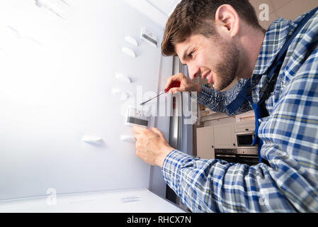 Male Worker Repairing Refrigerator With Hand Tool In Kitchen Room Stock Photo