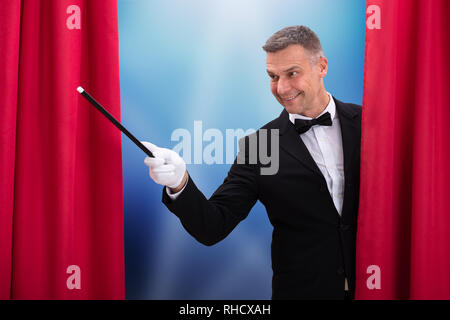 Front View Of Smiling Magician Holding Magic Wand Stock Photo